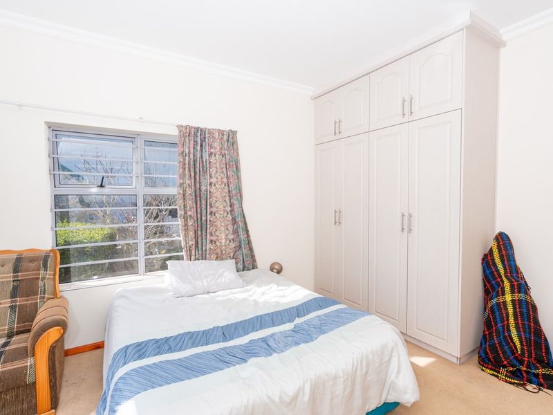 A bedroom featuring built-in cupboards, carpeted flooring, and a window fitted with security bars.