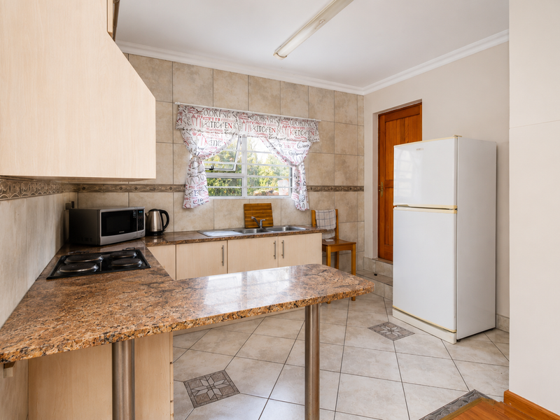 A functional kitchen featuring granite countertops, tiled flooring, built-in cabinetry, and an electric hob, providing a practical workspace with direct access to an exterior door.