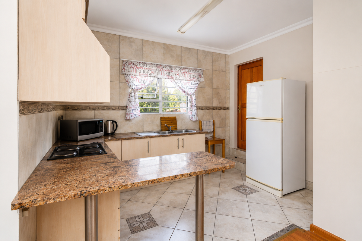 A functional kitchen featuring granite countertops, tiled flooring, built-in cabinetry, and an electric hob, providing a practical workspace with direct access to an exterior door.