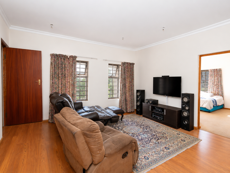 A spacious living room featuring laminate flooring, coved cornicing, and steel frame windows, with an open doorway leading to an adjacent bedroom.