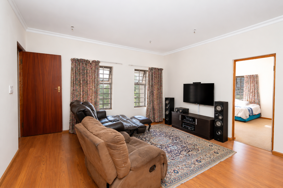A spacious living room featuring laminate flooring, coved cornicing, and steel frame windows, with an open doorway leading to an adjacent bedroom.