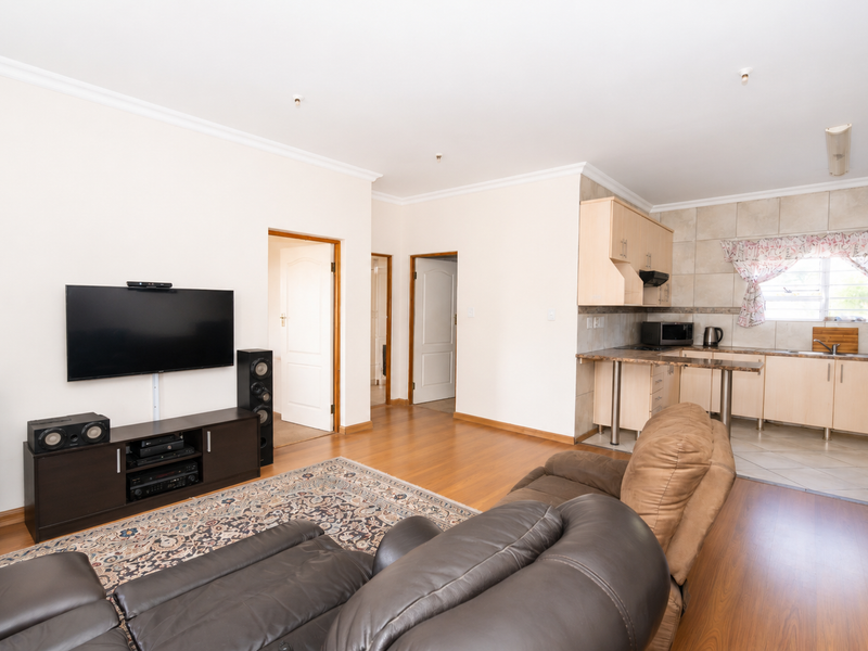Open-plan living area featuring laminate flooring, coved cornicing, and a functional kitchen with built-in cabinetry and tiled backsplash.