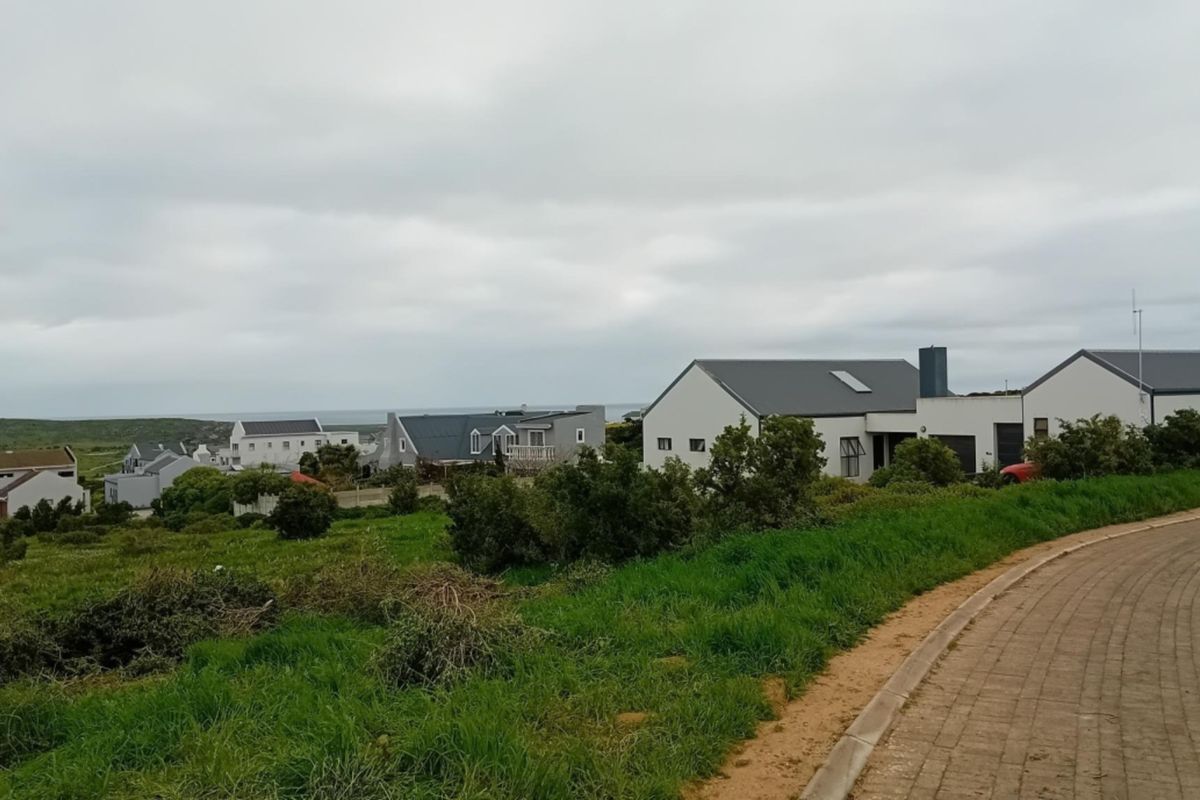 A scenic view of a coastal residential neighborhood featuring modern homes, paved roads, and natural green landscape under an overcast sky.