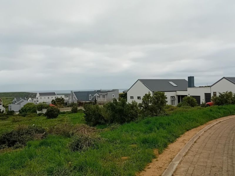 A scenic view of a coastal residential neighborhood featuring modern homes, paved roads, and natural green landscape under an overcast sky.