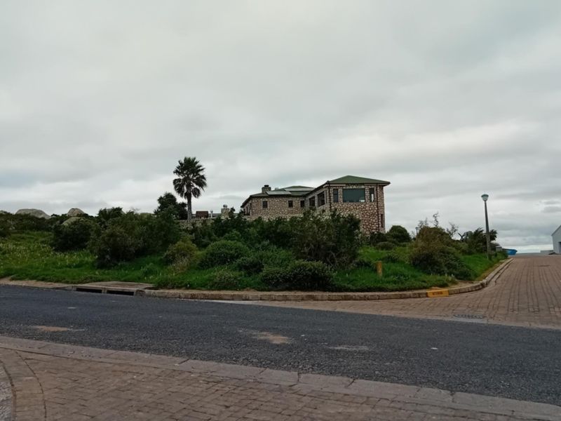 A street-level view of a residential property featuring stone-clad exterior walls and a pitched roof, situated on a corner lot with paved access.