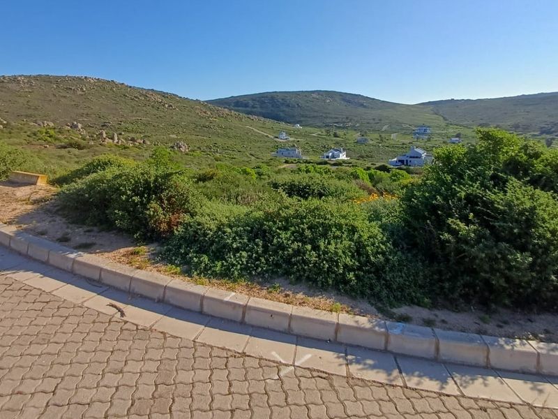 A view of a vacant residential plot featuring a paved driveway and concrete curbing, set against a natural hillside landscape.