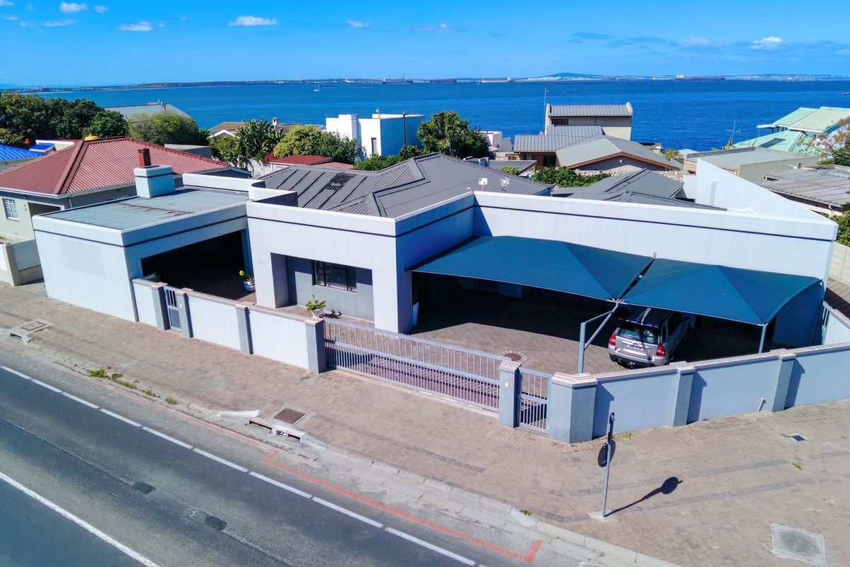 Aerial view of a coastal property featuring a paved driveway, secure perimeter walling, and a large shade sail carport structure.