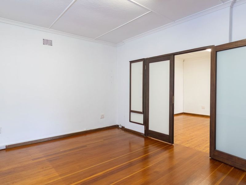 An empty living room featuring polished timber flooring and elegant frosted glass double doors leading to an adjacent space.