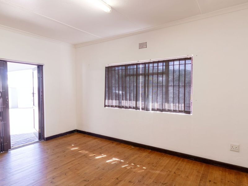 A bright, empty living room featuring timber flooring, a security gate leading outdoors, and vertical window blinds.