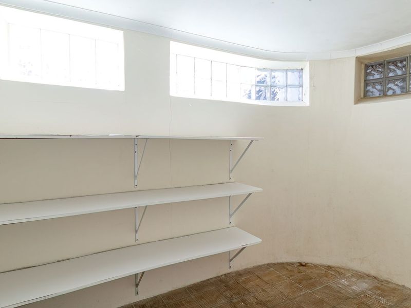 A functional utility space featuring wall-mounted shelving, glass block windows, and tiled flooring, offering potential for storage or a dedicated workspace.