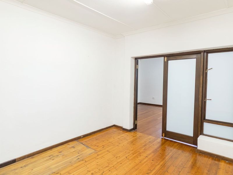 An empty living room featuring polished hardwood flooring, coved ceilings, and a frosted glass panel door leading to an adjacent space.