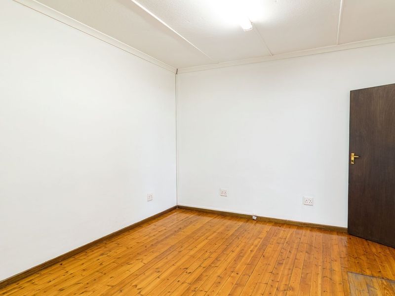 An empty bedroom featuring polished timber flooring, white walls, and a dark wood door.