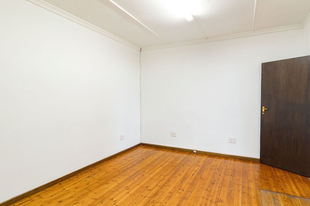 An empty bedroom featuring polished timber flooring, white walls, and a dark wood door.