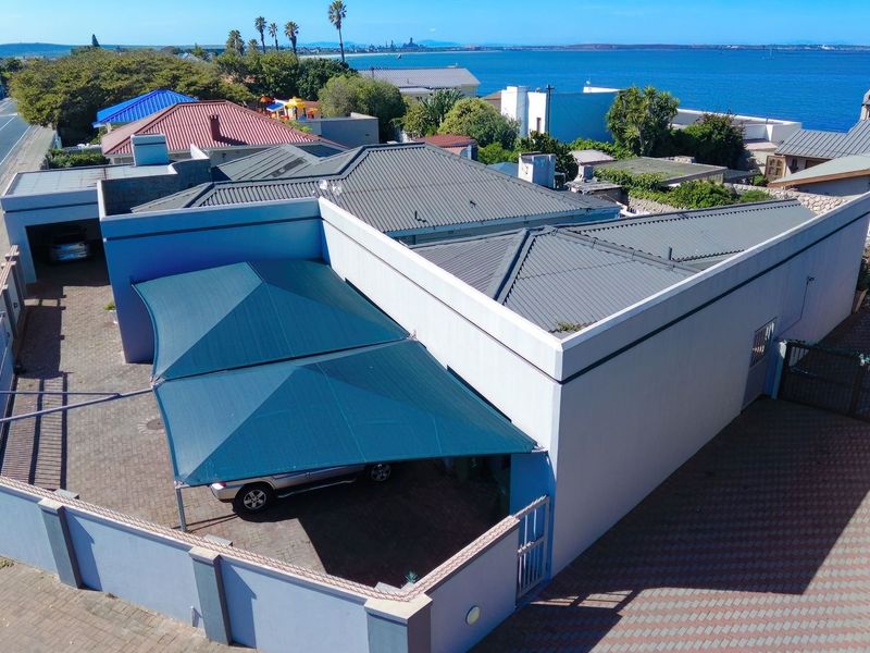 Aerial view of the property featuring a paved driveway, shade sail carport, and secure perimeter wall, situated near the coastline.