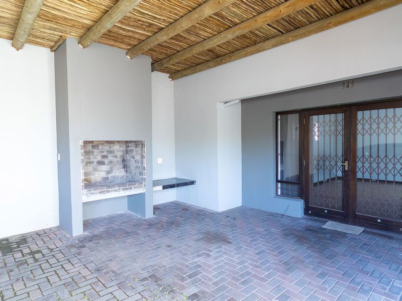 A covered patio area featuring a built-in braai, rustic thatched ceiling, and durable brick paving, providing a functional outdoor entertainment space.