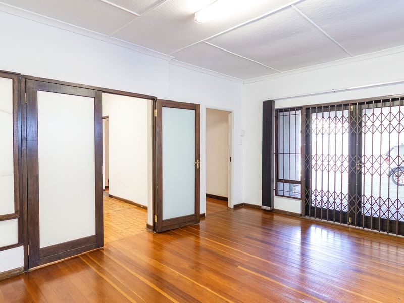 Spacious living area featuring polished hardwood flooring, secure sliding doors with metal security gates, and classic frosted glass interior doors.