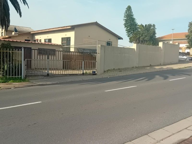 Street view of the property showing the front facade, perimeter wall, and metal driveway gate access from the road.