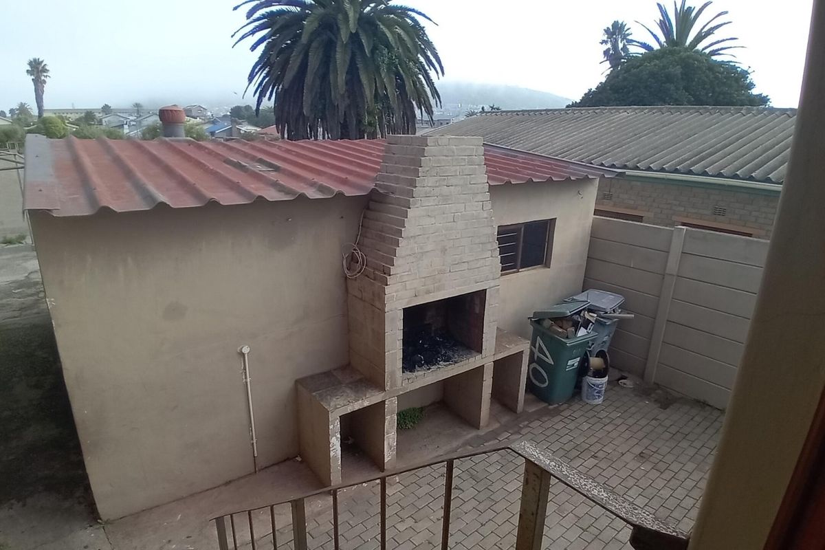 Rear courtyard area featuring a built-in brick braai, paved flooring, and a corrugated metal roof structure.