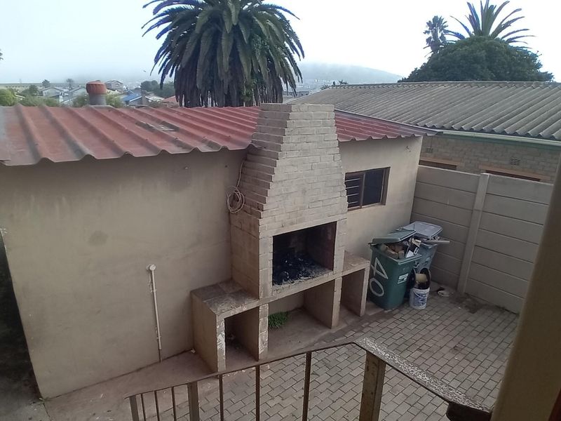 Rear courtyard area featuring a built-in brick braai, paved flooring, and a corrugated metal roof structure.