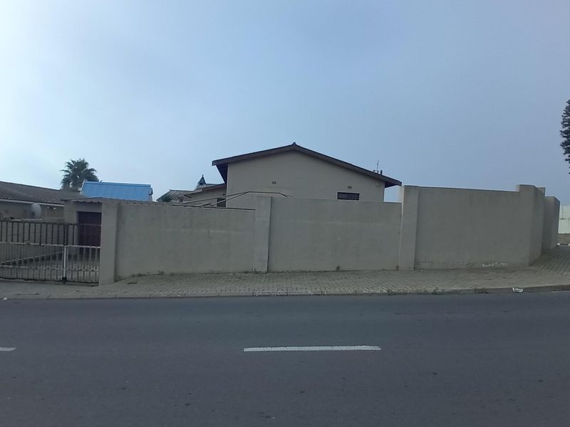 Street view of the property showing the perimeter wall, metal gate, and adjacent paved sidewalk.