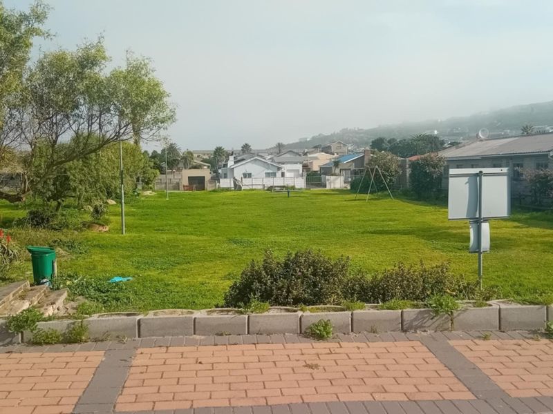 A spacious, level grass garden area featuring a paved walkway and low retaining wall, offering an open outdoor space.