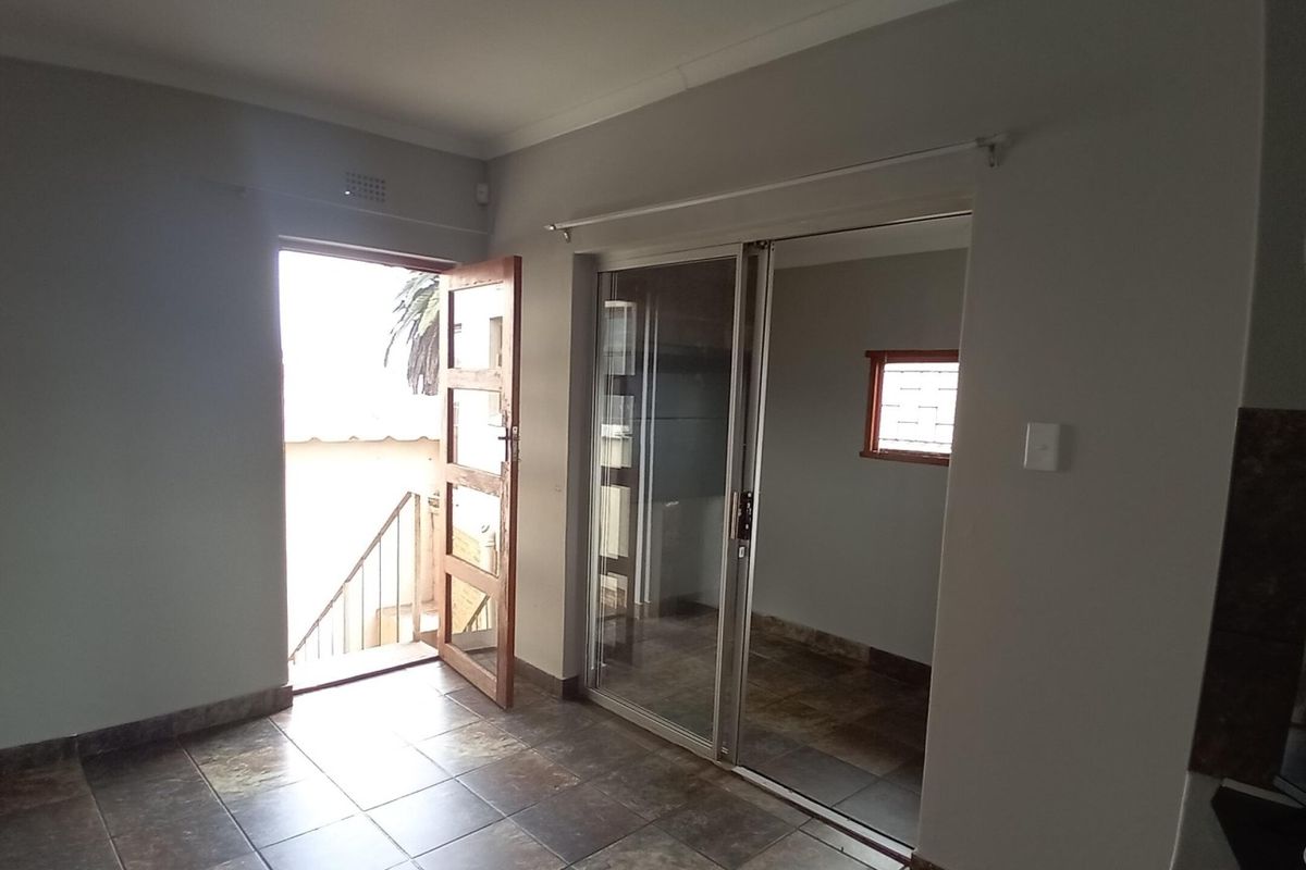 An empty living area featuring tiled flooring, a sliding glass door leading to an adjacent space, and an external timber door.