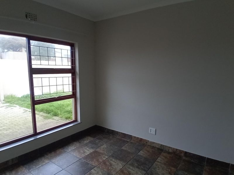 An empty bedroom featuring tiled flooring, a large window with security bars, and neutral wall finishes.
