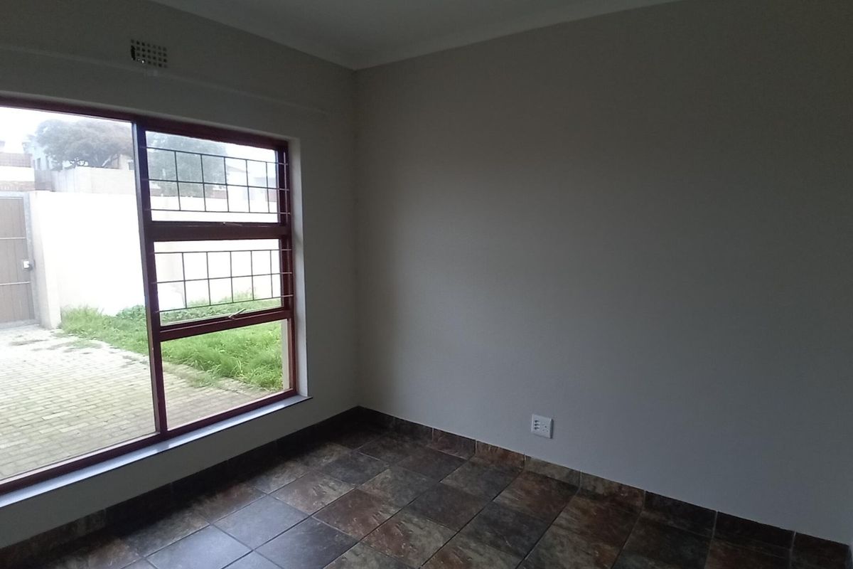 An empty bedroom featuring tiled flooring, a large window with security bars, and neutral wall finishes.