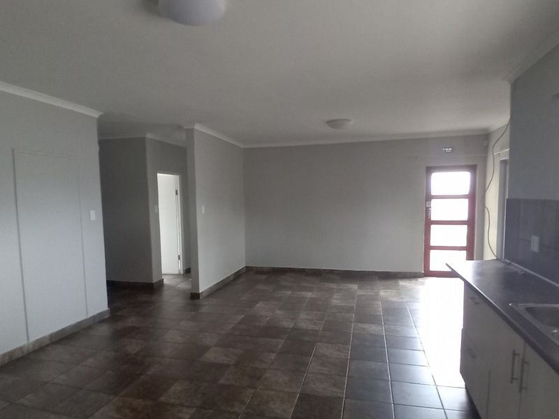 An open-plan living and kitchen area featuring tiled flooring, neutral walls, and functional kitchen cabinetry with a double bowl sink.