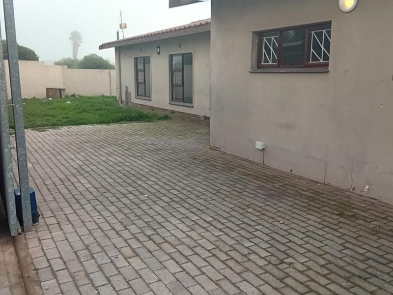 Rear exterior view of the property featuring a paved courtyard area, boundary wall, and security bars on the windows.
