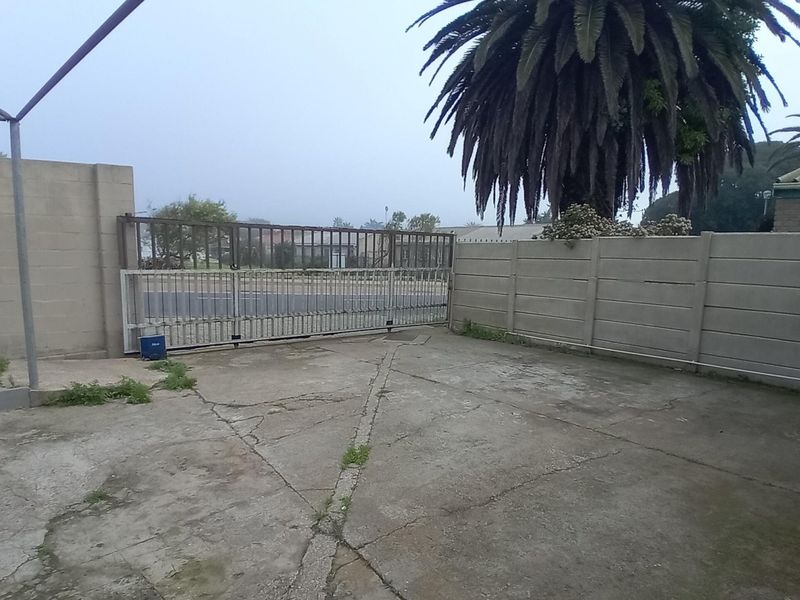A paved driveway area featuring a sliding metal gate, enclosed by precast concrete boundary walls and a metal support structure.