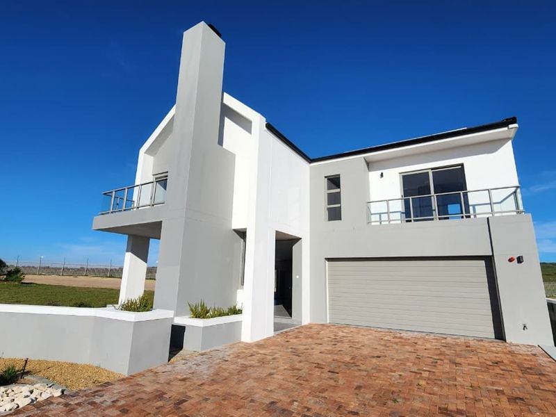 Modern double-story residential home featuring a brick paved driveway, double garage, and upper-level balconies with glass balustrades.