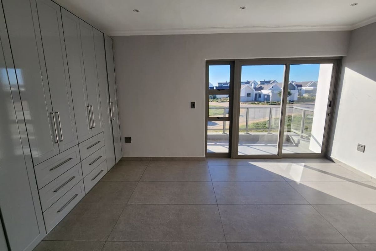 A bright, modern bedroom featuring extensive built-in cupboards, large format floor tiles, and direct access to a private balcony through sliding glass doors.