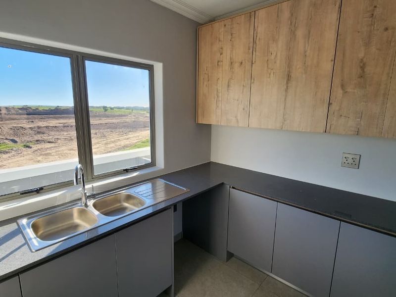 A modern, clean scullery featuring double bowl stainless steel sink, stone countertops, and ample laminate cabinetry with a view of the surrounding landscape.