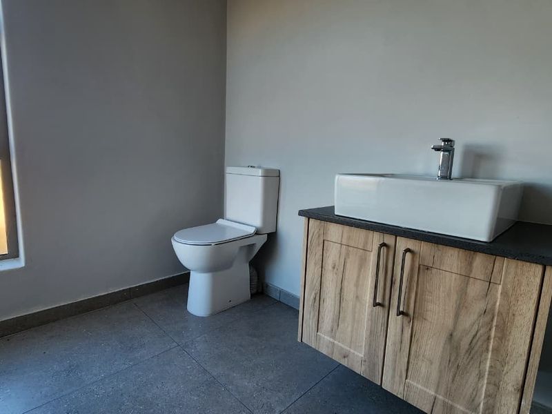 A clean, modern bathroom featuring a wood-finish vanity with a vessel sink, a white toilet, and large-format floor tiles.
