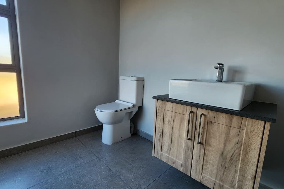 A clean, modern bathroom featuring a wood-finish vanity with a vessel sink, a white toilet, and large-format floor tiles.