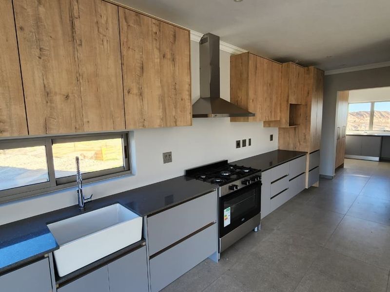 Modern kitchen featuring wood-grain and grey cabinetry, stone countertops, a farmhouse sink, and a gas stove with an extractor fan.