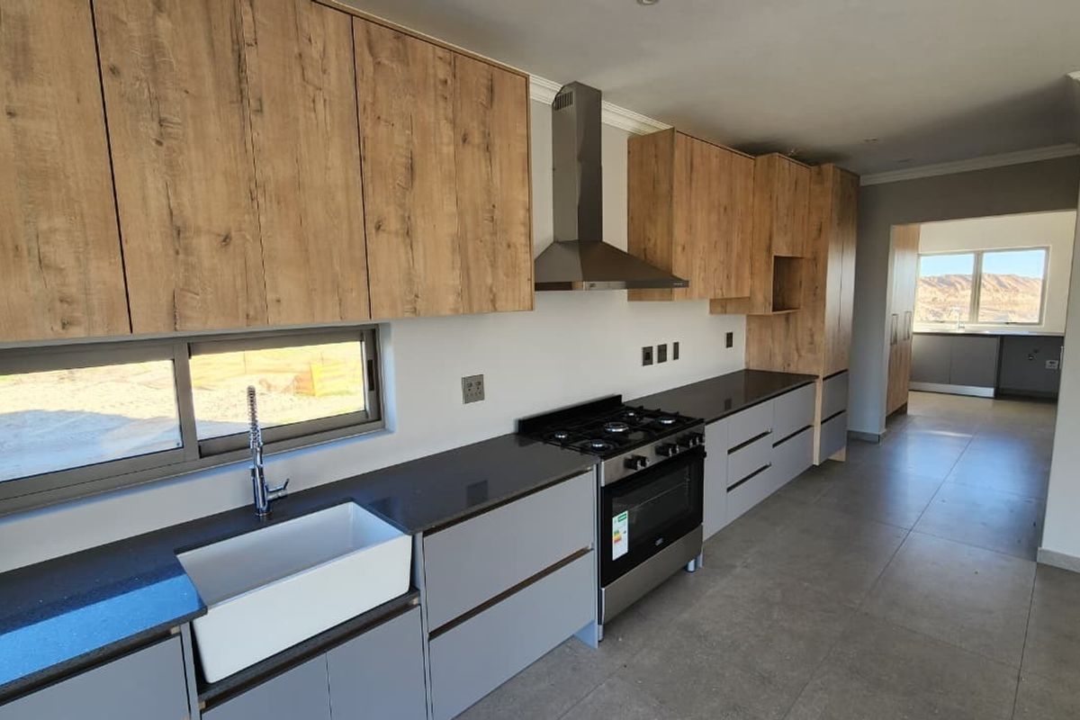 Modern kitchen featuring wood-grain and grey cabinetry, stone countertops, a farmhouse sink, and a gas stove with an extractor fan.