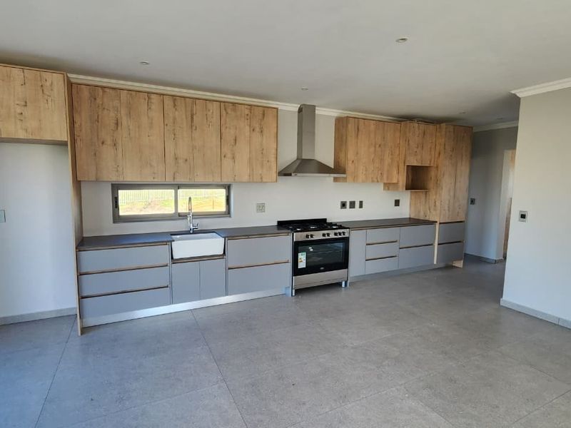 Modern kitchen featuring wood-look and grey cabinetry, a farmhouse-style apron sink, stainless steel extractor fan, and a gas stove with tiled flooring.