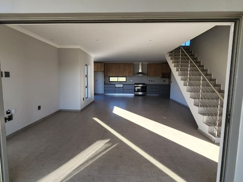 Spacious open-plan living and kitchen area featuring modern cabinetry, a stainless steel stove, and a contemporary staircase with a sleek balustrade.