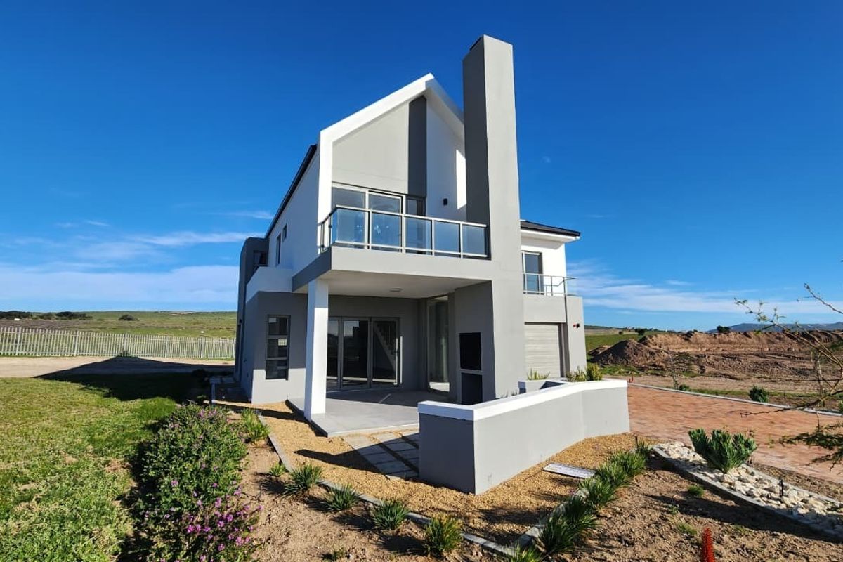 Modern double-story rear elevation featuring a covered patio with built-in braai, a first-floor balcony with glass balustrades, and contemporary architectural finishes.