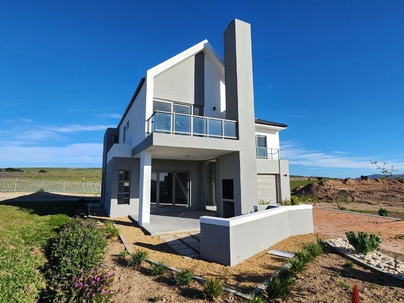 Modern double-story rear elevation featuring a covered patio with built-in braai, a first-floor balcony with glass balustrades, and contemporary architectural finishes.