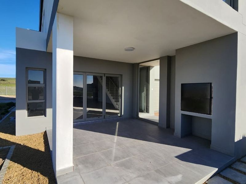 A modern covered patio featuring tiled flooring, a built-in braai, and large sliding glass doors providing seamless access to the interior living space.