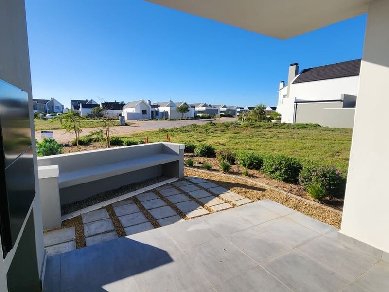 A covered patio featuring tiled flooring, a built-in concrete bench, and a built-in braai, overlooking a landscaped garden and neighborhood.