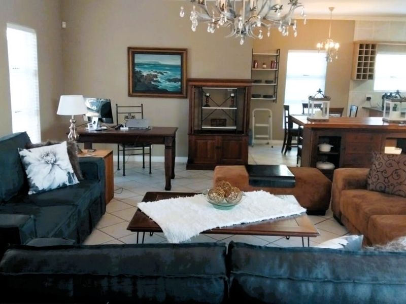 Spacious open-plan living area featuring tiled flooring, a central chandelier, and a connected kitchen with built-in cabinetry and an island.