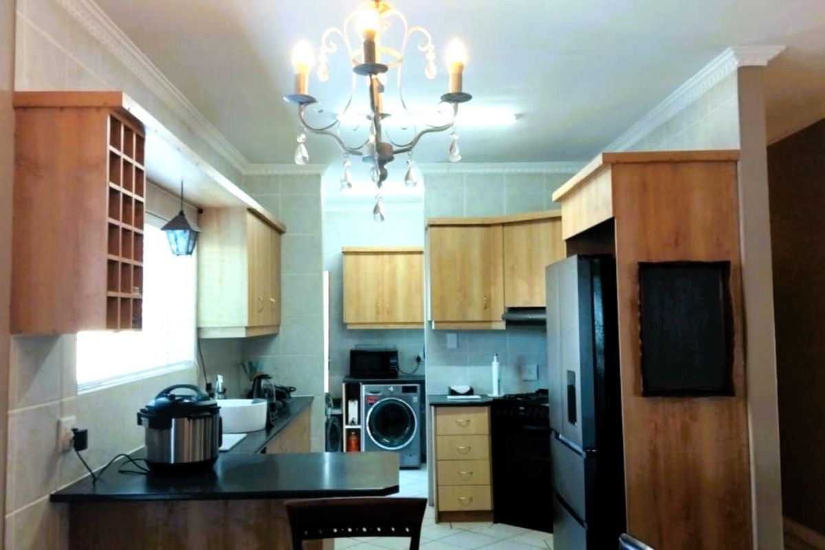 A functional kitchen featuring light wood cabinetry, dark countertops, tiled backsplash, and a central chandelier, offering a practical layout for daily meal preparation.