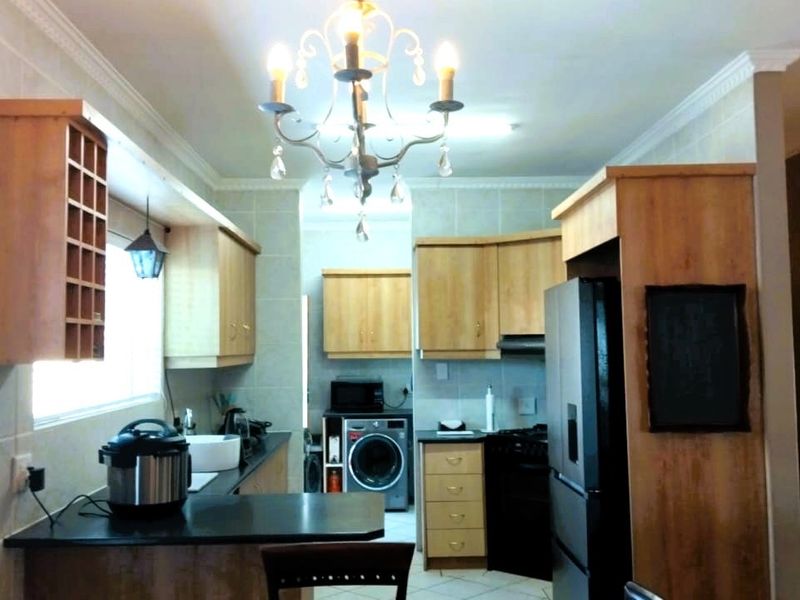 A functional kitchen featuring light wood cabinetry, dark countertops, tiled backsplash, and a central chandelier, offering a practical layout for daily meal preparation.