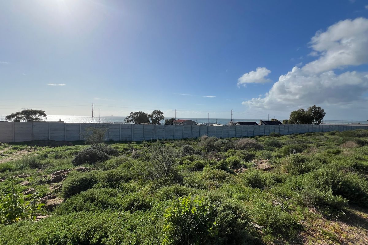 A vacant residential plot featuring natural vegetation and a precast concrete boundary wall, offering a view towards the distant coastline.