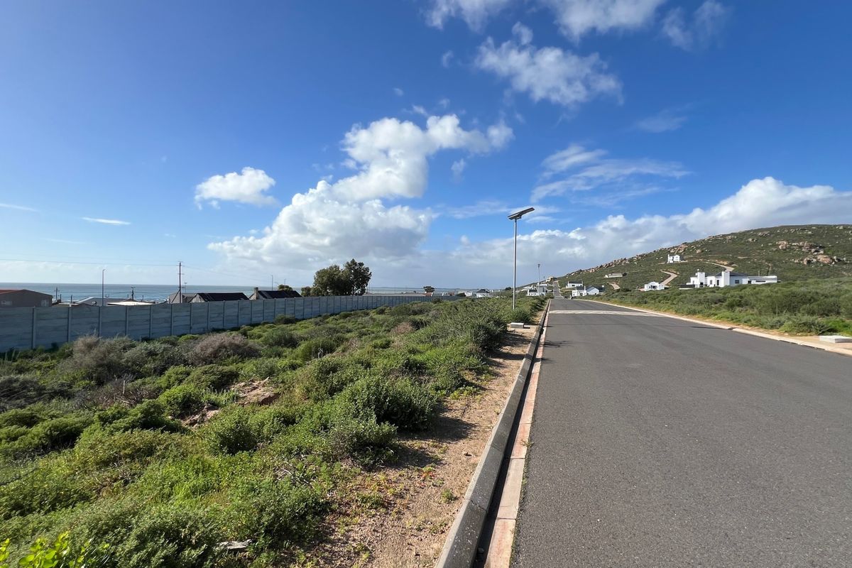 A view of the paved street frontage adjacent to the vacant residential plot, featuring a boundary wall and solar street lighting.