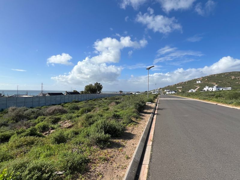 A view of the paved street frontage adjacent to the vacant residential plot, featuring a boundary wall and solar street lighting.